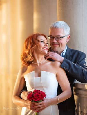 Elegant wedding portrait with couple posing by classical columns in warm lighting.