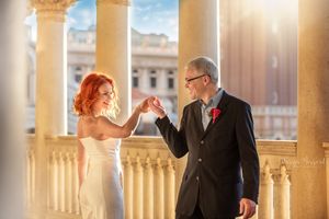 Wedding couple holds hands in joyful moment between elegant columned architecture.