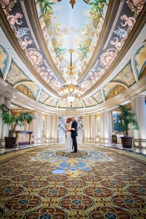 Elegant ballroom with painted ceiling, crystal chandelier and ornate carpet featuring a romantic dance moment.