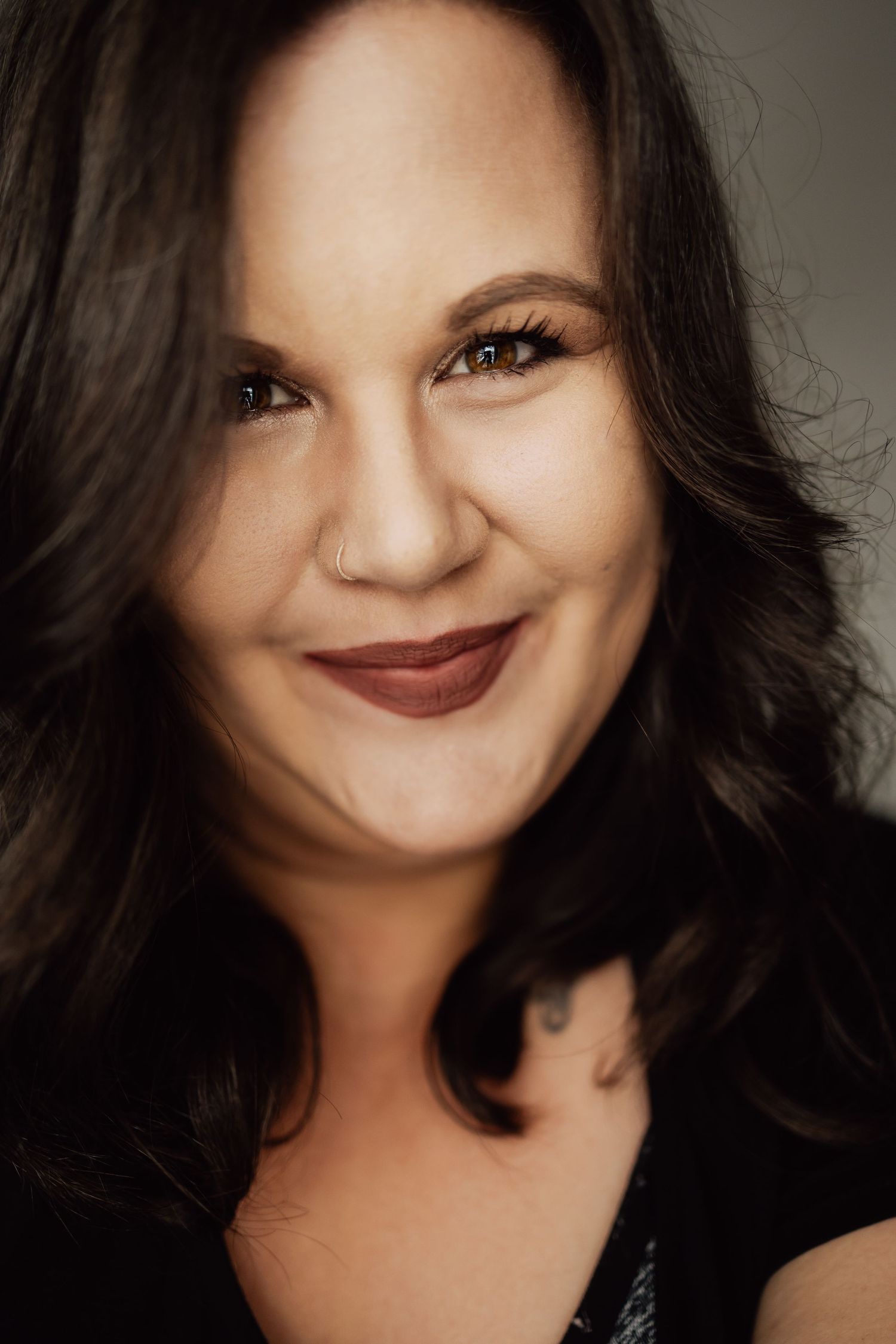 Warm portrait with natural makeup and dark wavy hair against neutral background.