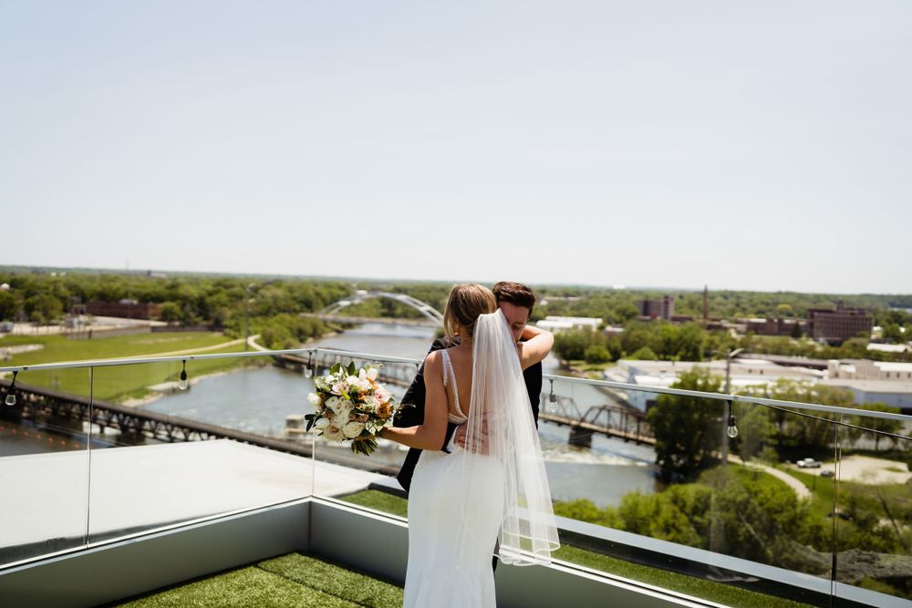 A couple stands together on a rooftop terrace overlooking a scenic river landscape.
