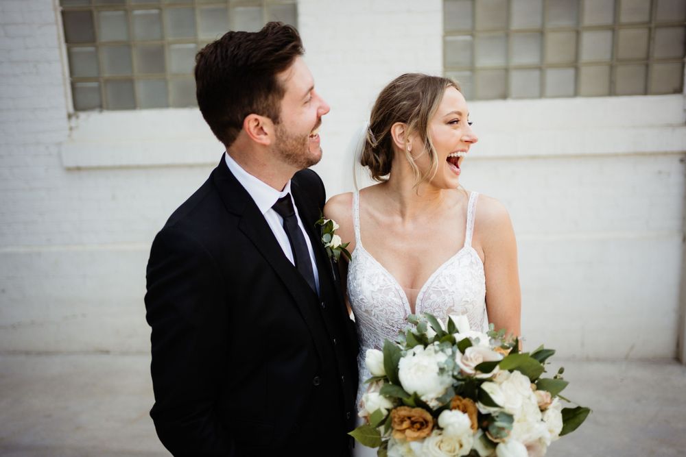 A wedding couple shares a joyful moment together while holding a floral bouquet.