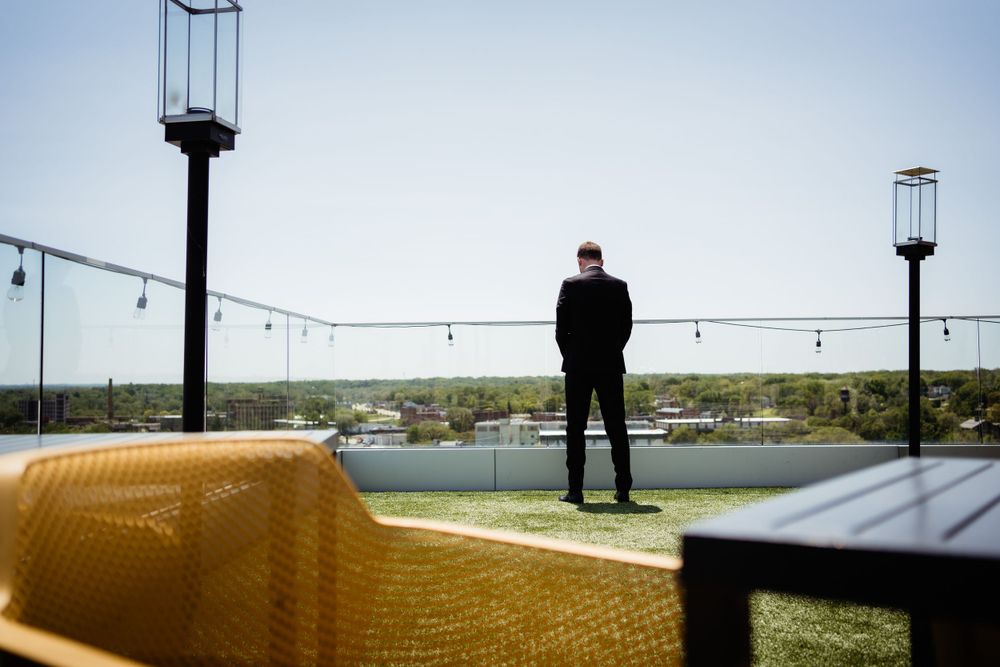 A silhouette stands on a rooftop overlooking a waterfront view with string lights and a yellow bench.