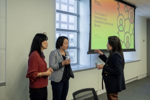Professional women having a discussion by a window with presentation screen visible.