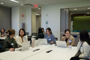 A group of professionals collaborate around a table with laptops during a meeting in a bright office space.