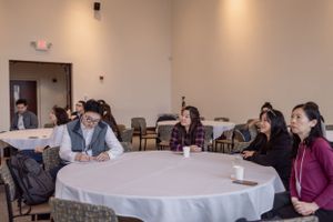 Professional conference room with round tables and attendees during a business presentation.