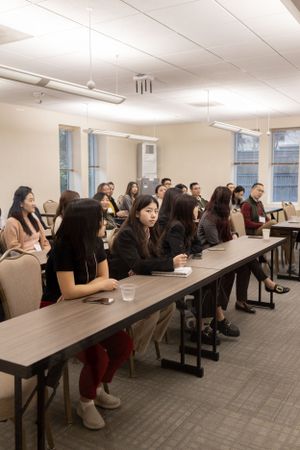 Students seated in rows at long tables in a classroom setting during a presentation or lecture.