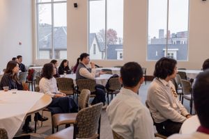 Meeting room with large windows showing city views and attendees seated at tables.