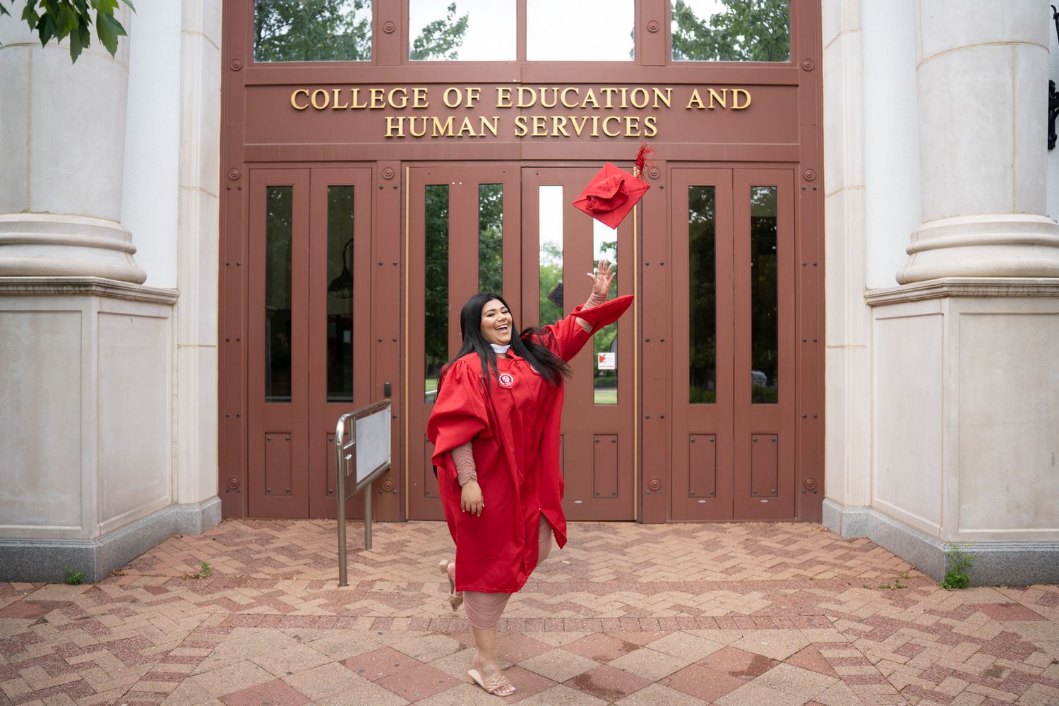 Red-robed graduate taking photos in front of collegiate building with classical columns.