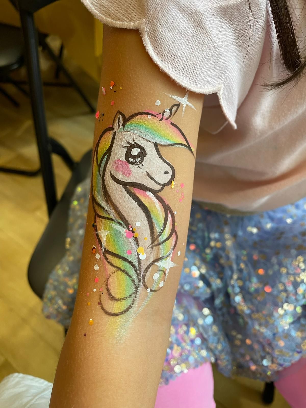 Pastel unicorn face paint design with sparkles and rainbow mane.