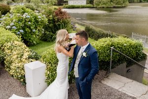 A wedding couple sharing an intimate moment by a lake surrounded by lush greenery.