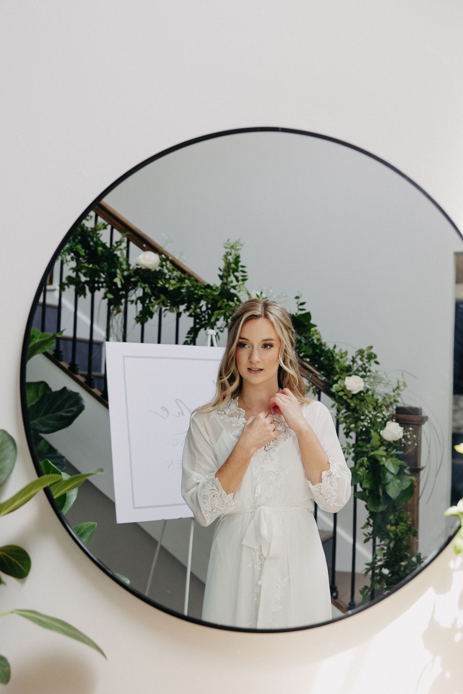 Circular mirror reflecting interior space with greenery and staircase.
