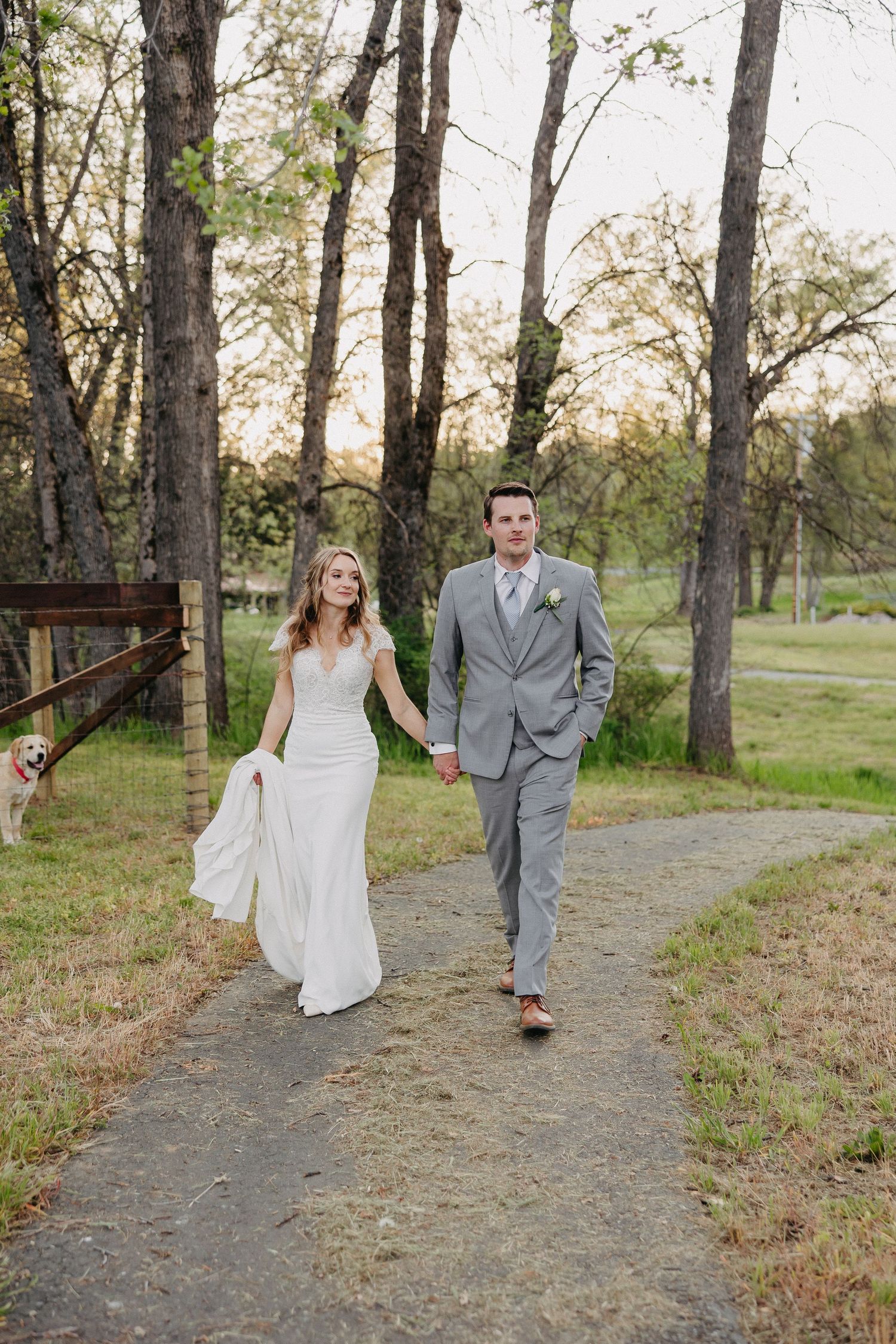 Newlyweds stroll together on garden path surrounded by trees during spring wedding.