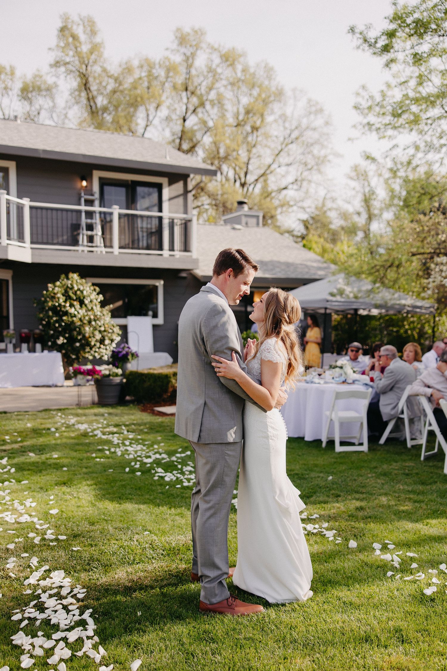 Wedding couple shares dance on lawn with reception tables and house in background.