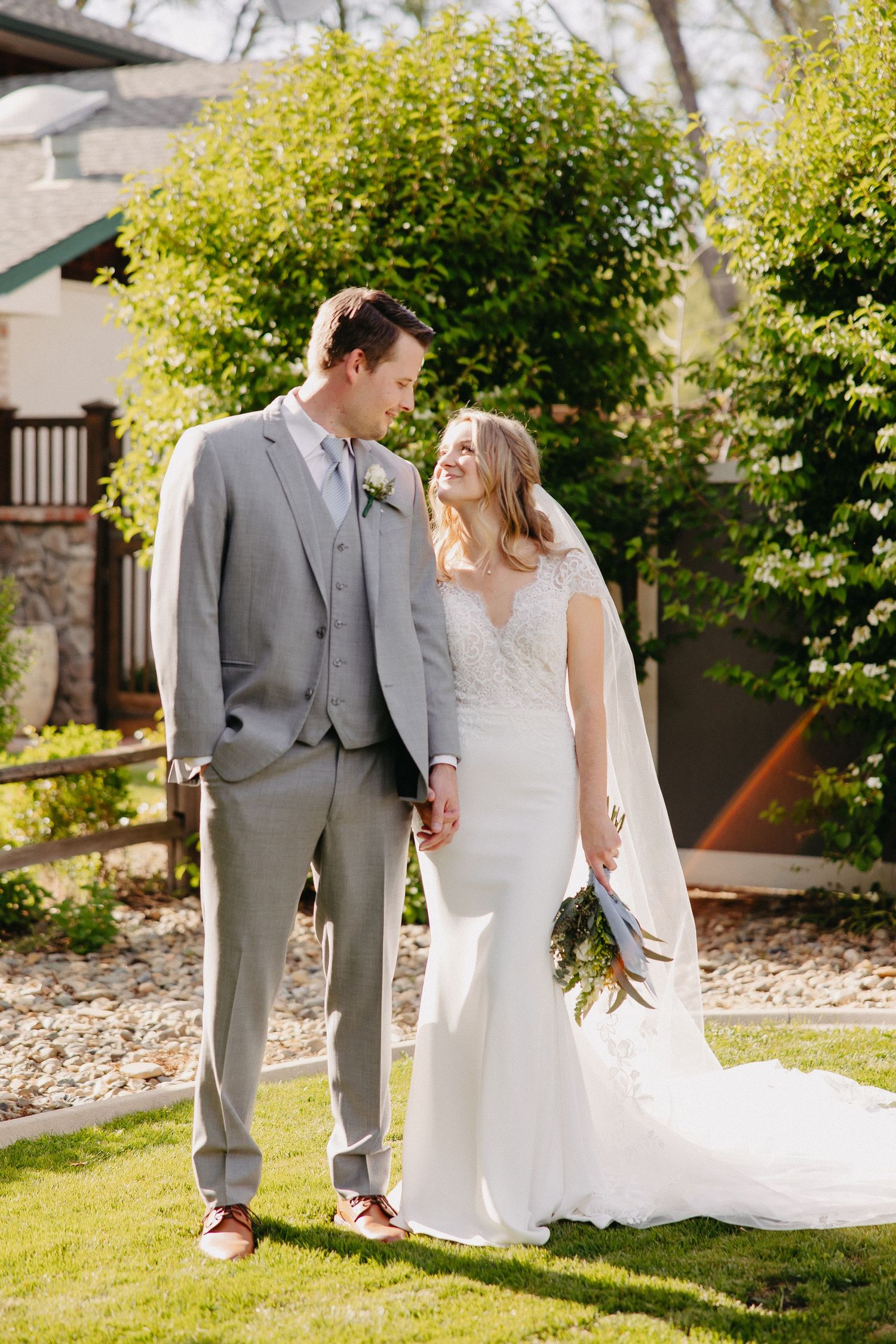 A joyful wedding couple holding hands on a sunny day with lush greenery in the background.