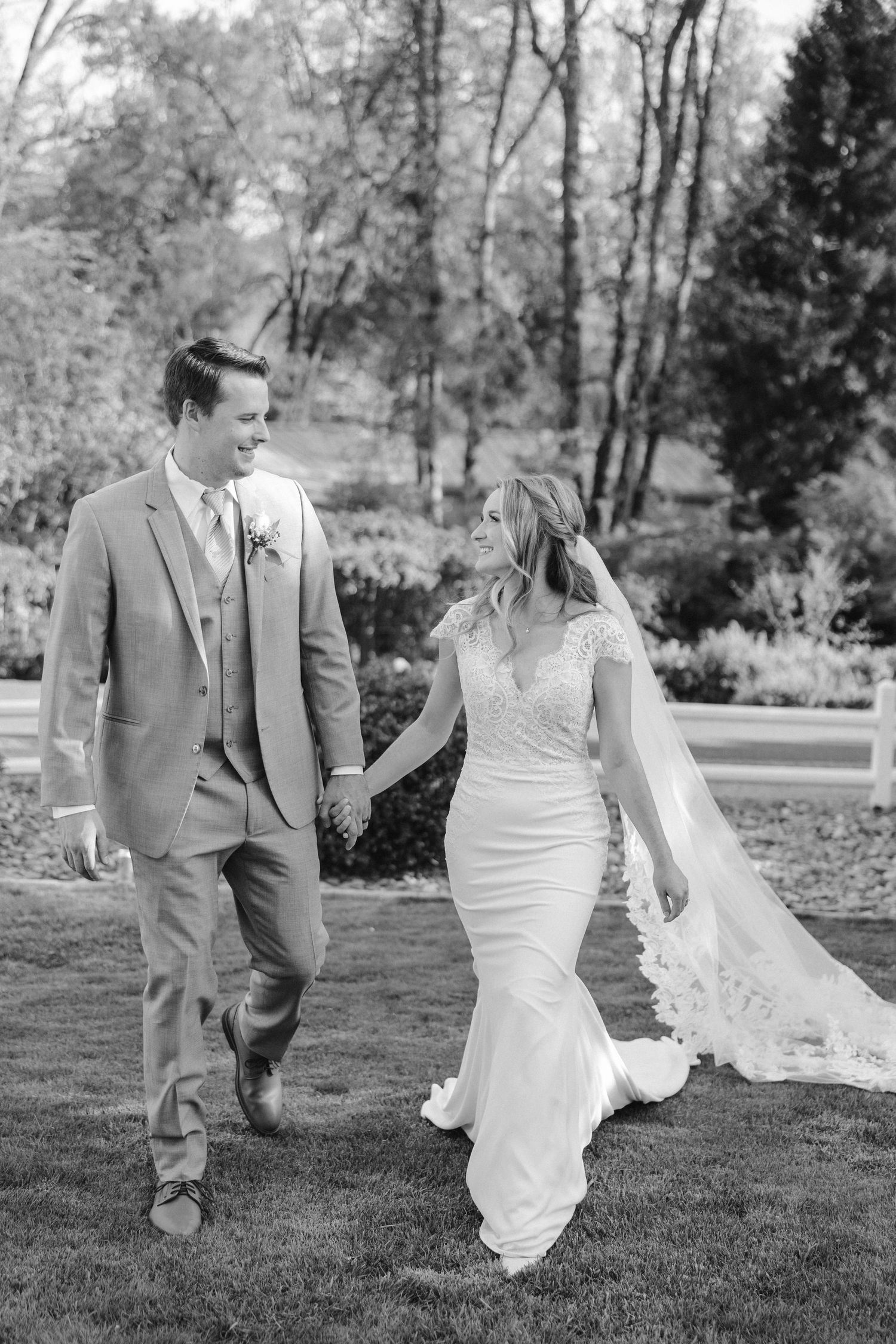 A black and white candid photo of a wedding couple walking together on garden grounds.