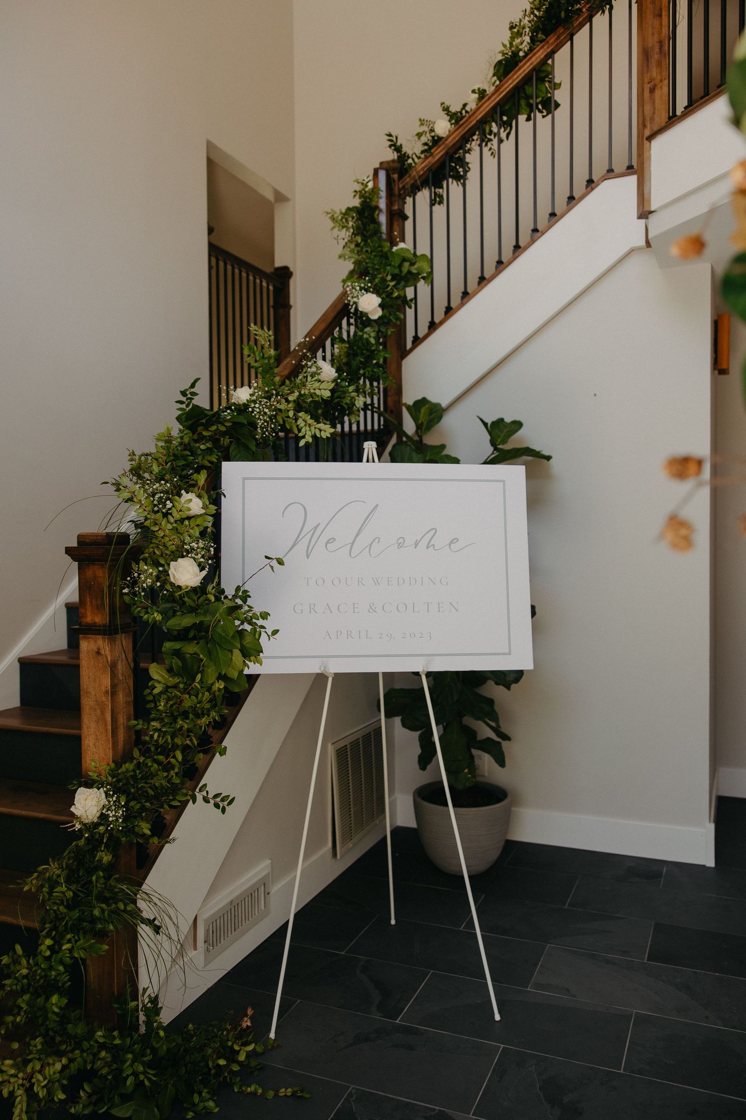 Welcome sign on easel with elegant greenery decorating staircase railings.