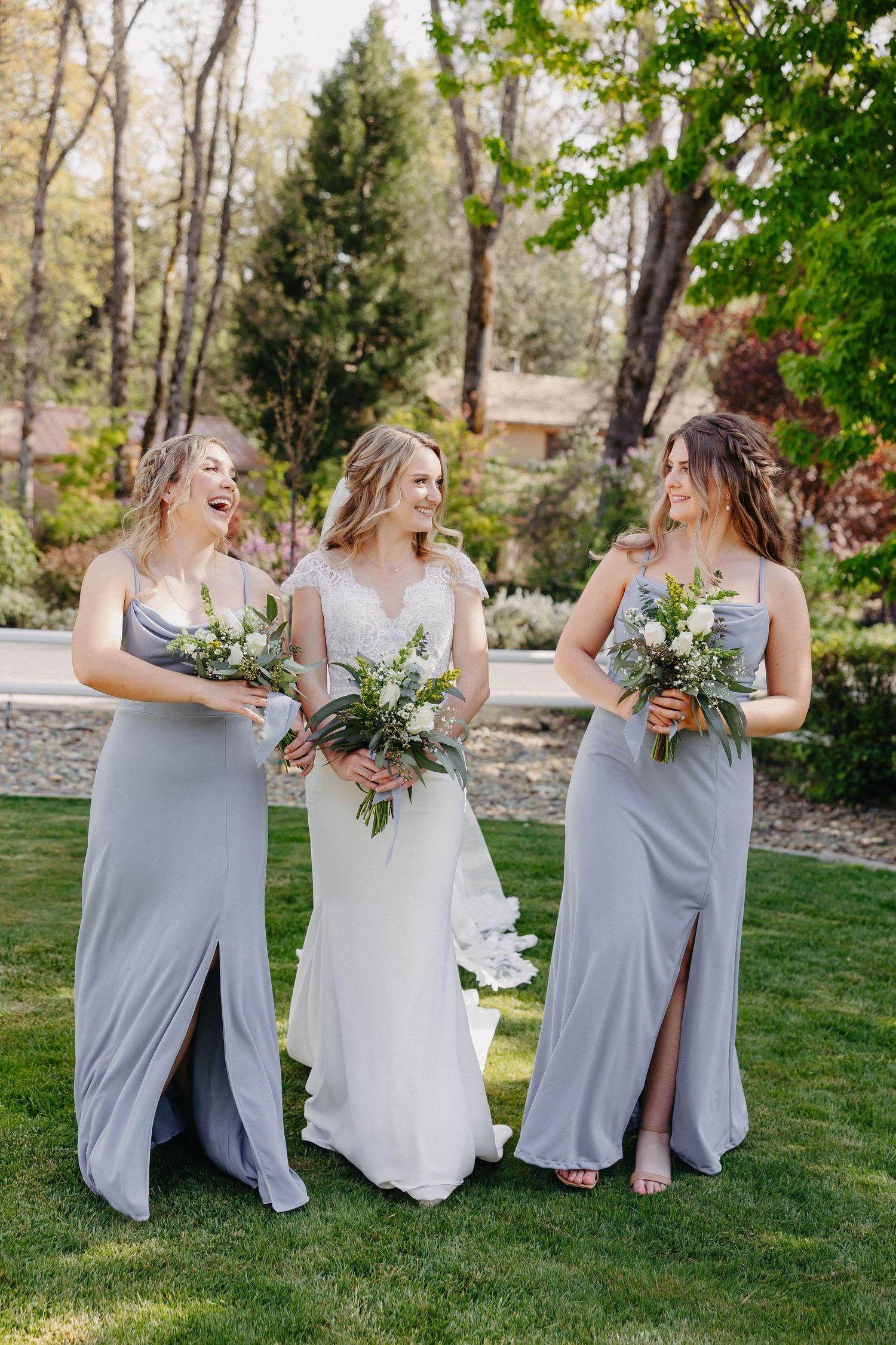 Three women in formal dresses share a joyful moment while holding green and white bouquets.