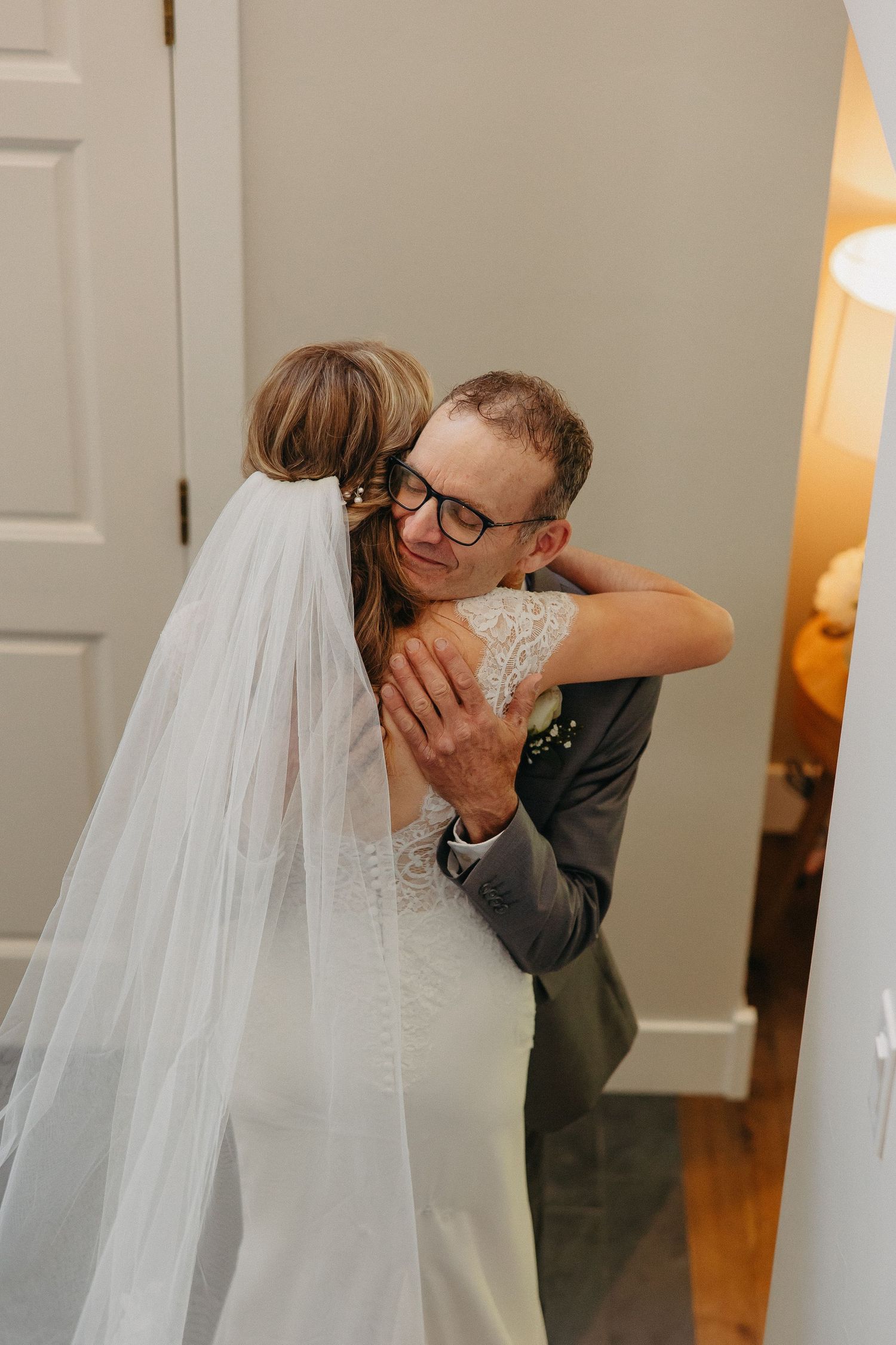 Two people embrace in an emotional moment on their wedding day, with the bride wearing a flowing white gown and veil.