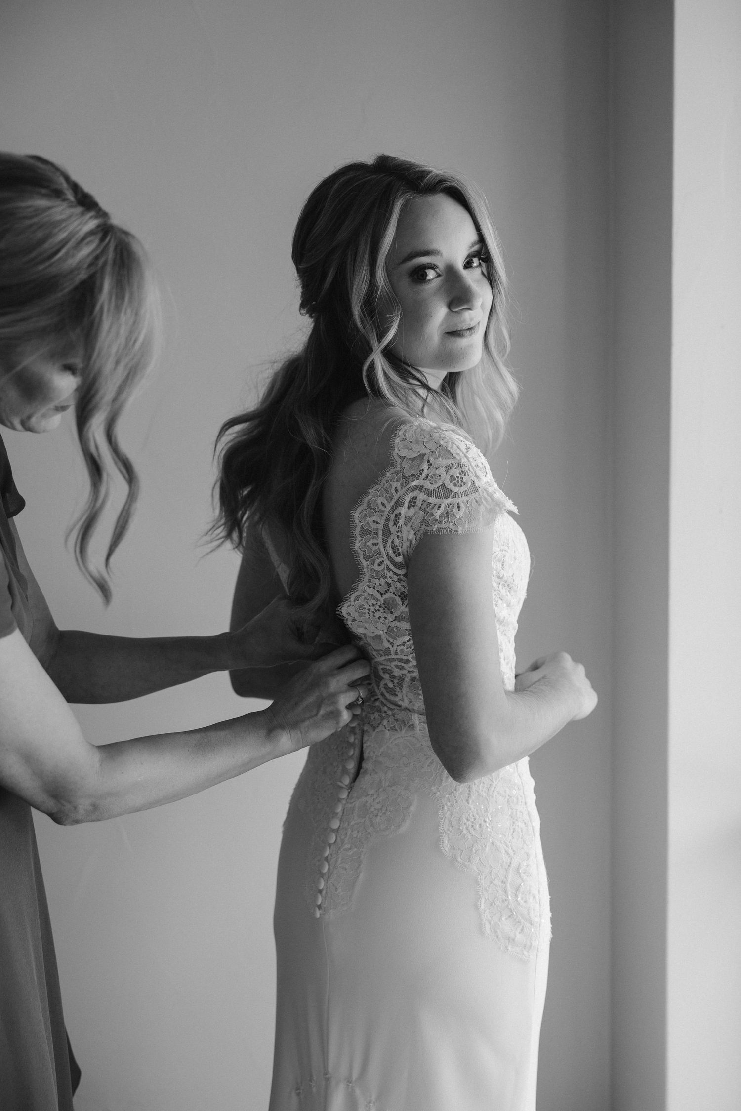 Wedding dress preparation scene showing detailed lace cap sleeves and elegant form-fitting silhouette in black and white.