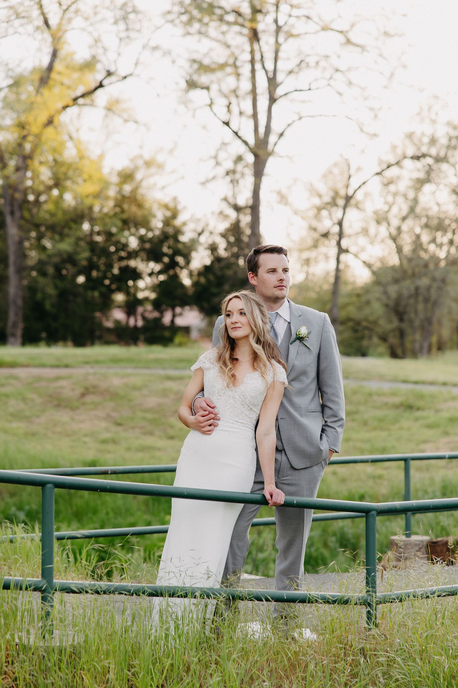Wedding couple poses against green railing in natural outdoor setting.