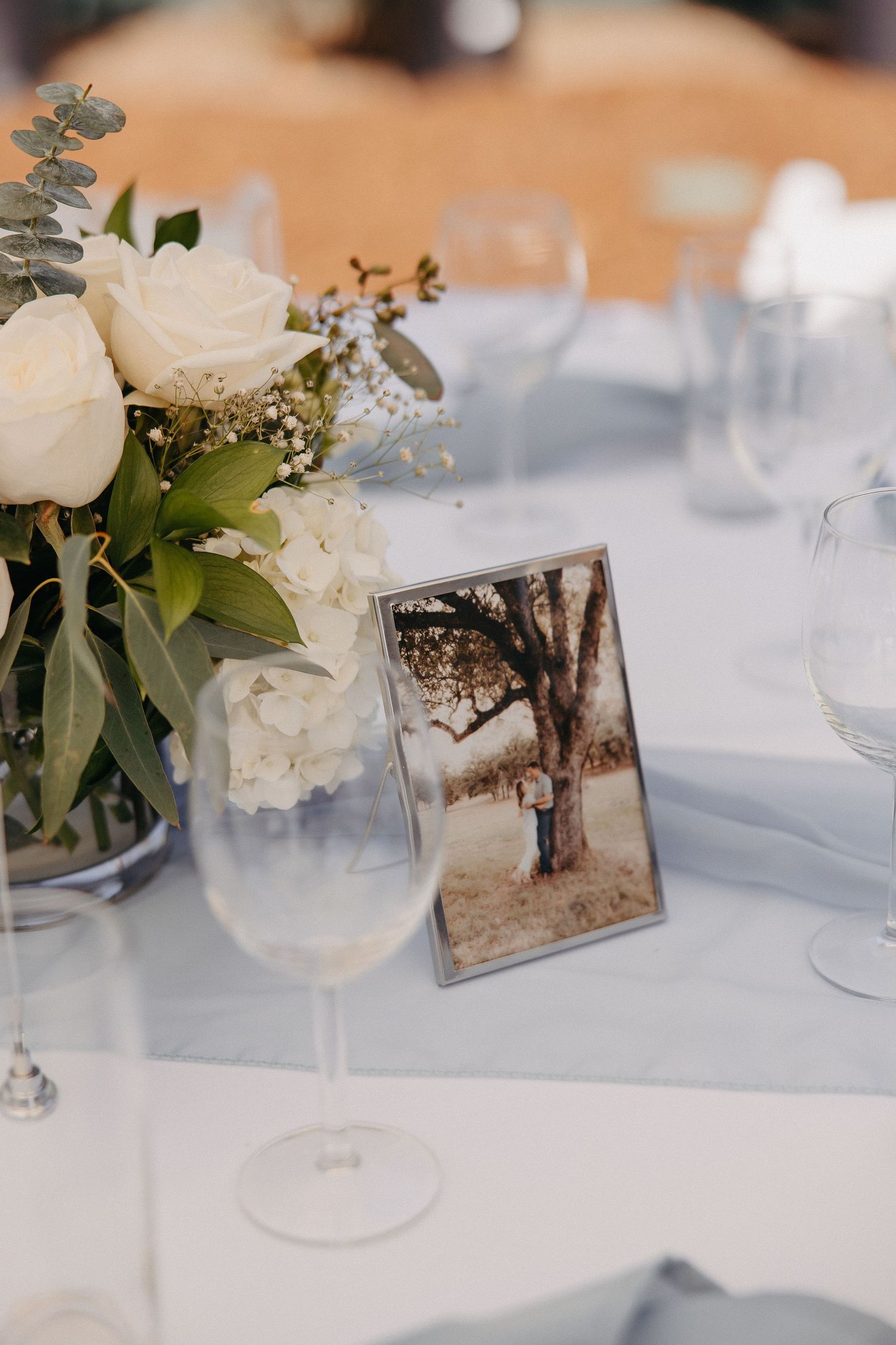 Elegant table setting with white floral centerpiece and framed photo near wine glass.