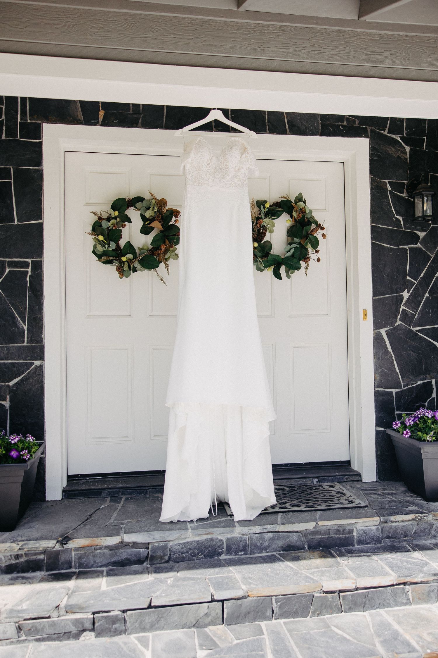 Wedding dress hanging on white door with matching evergreen wreaths.