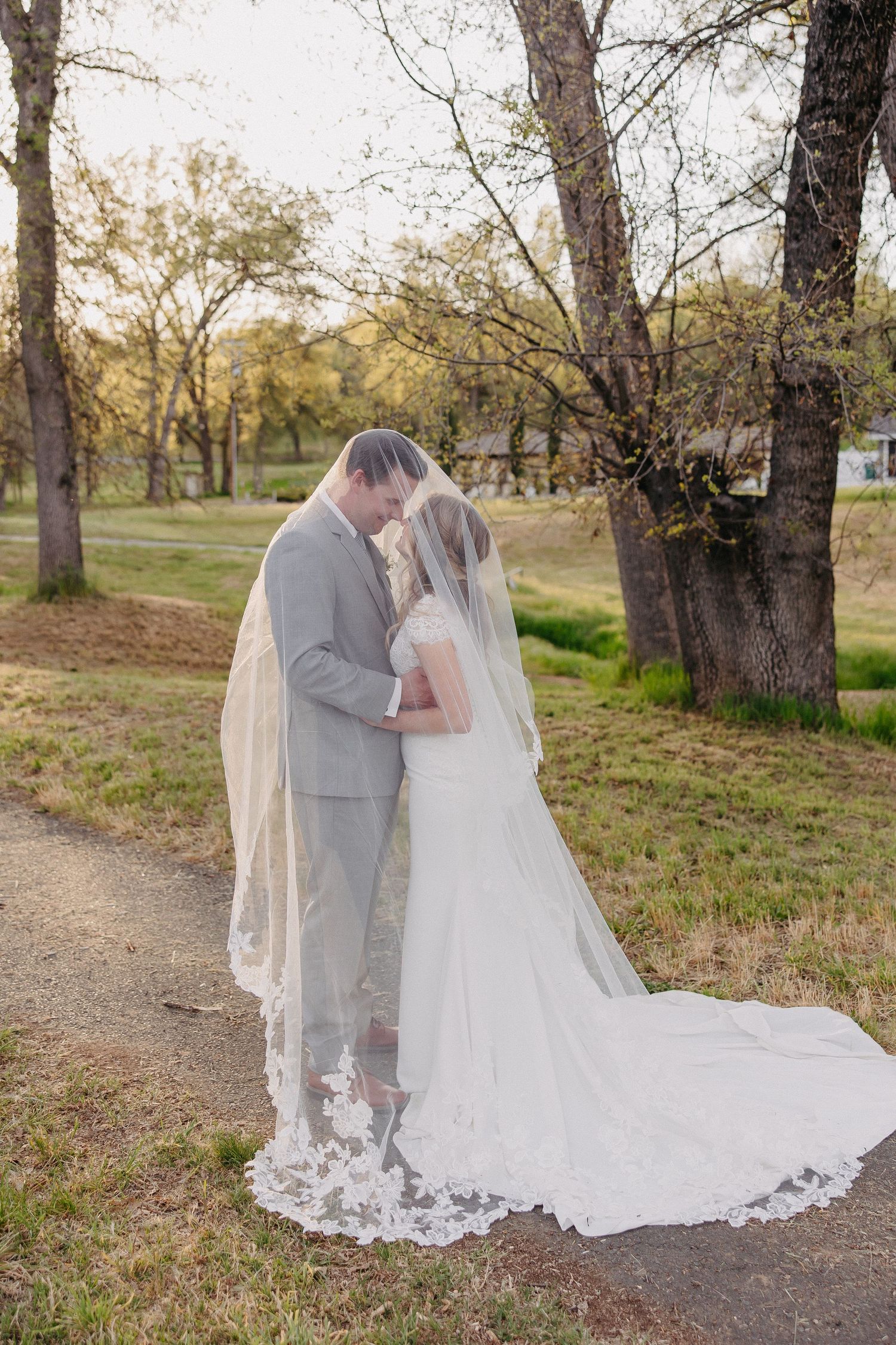 Wedding couple in gray suit and lace gown standing together on a trail at golden hour.