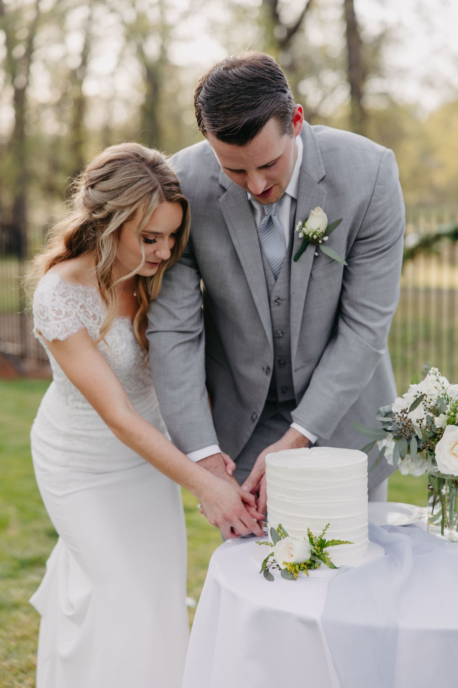 Newlyweds cutting their elegant white wedding cake together at outdoor garden reception.