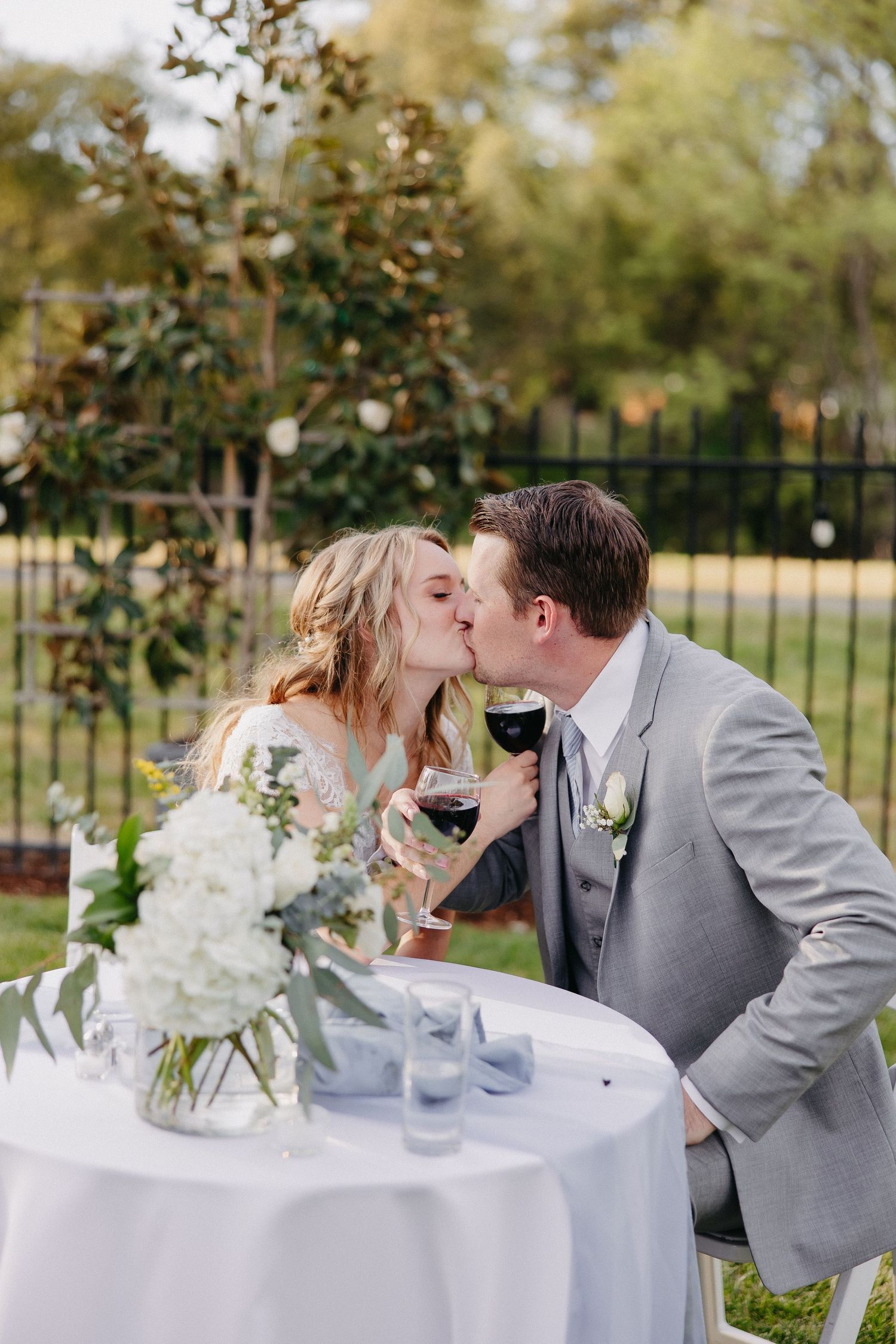 Couple sharing wine and intimate moment at wedding reception table with white floral centerpiece.