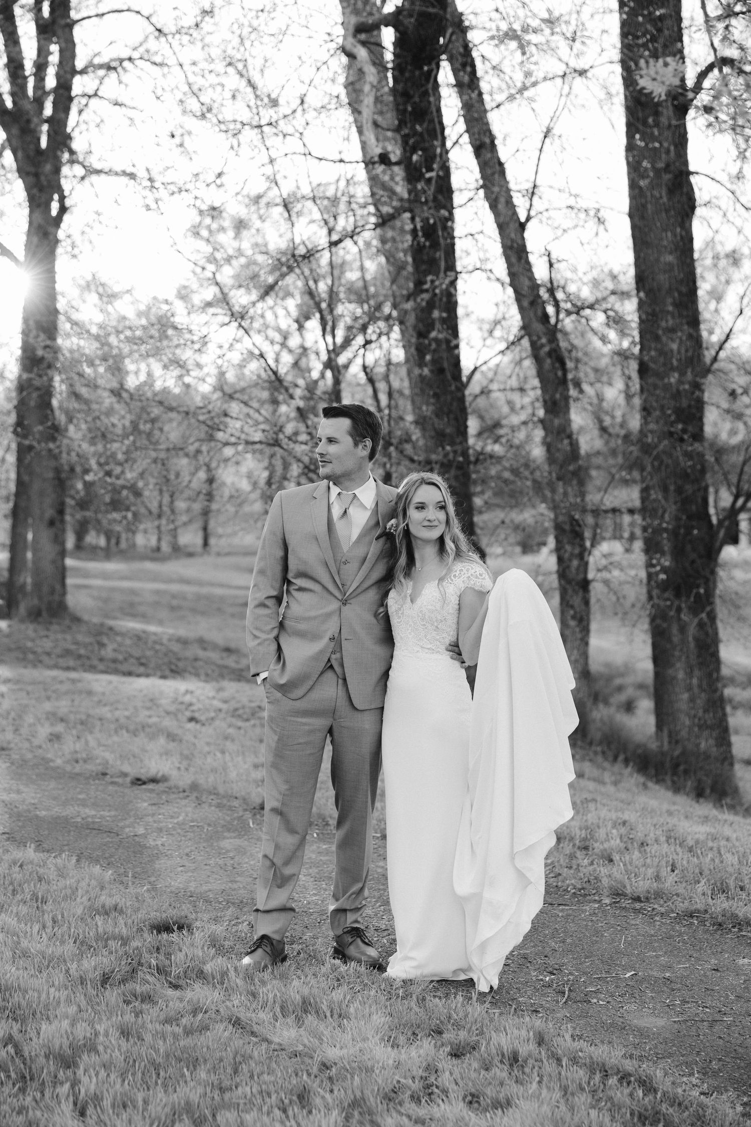 Black and white portrait of newlyweds standing together on a wooded trail.