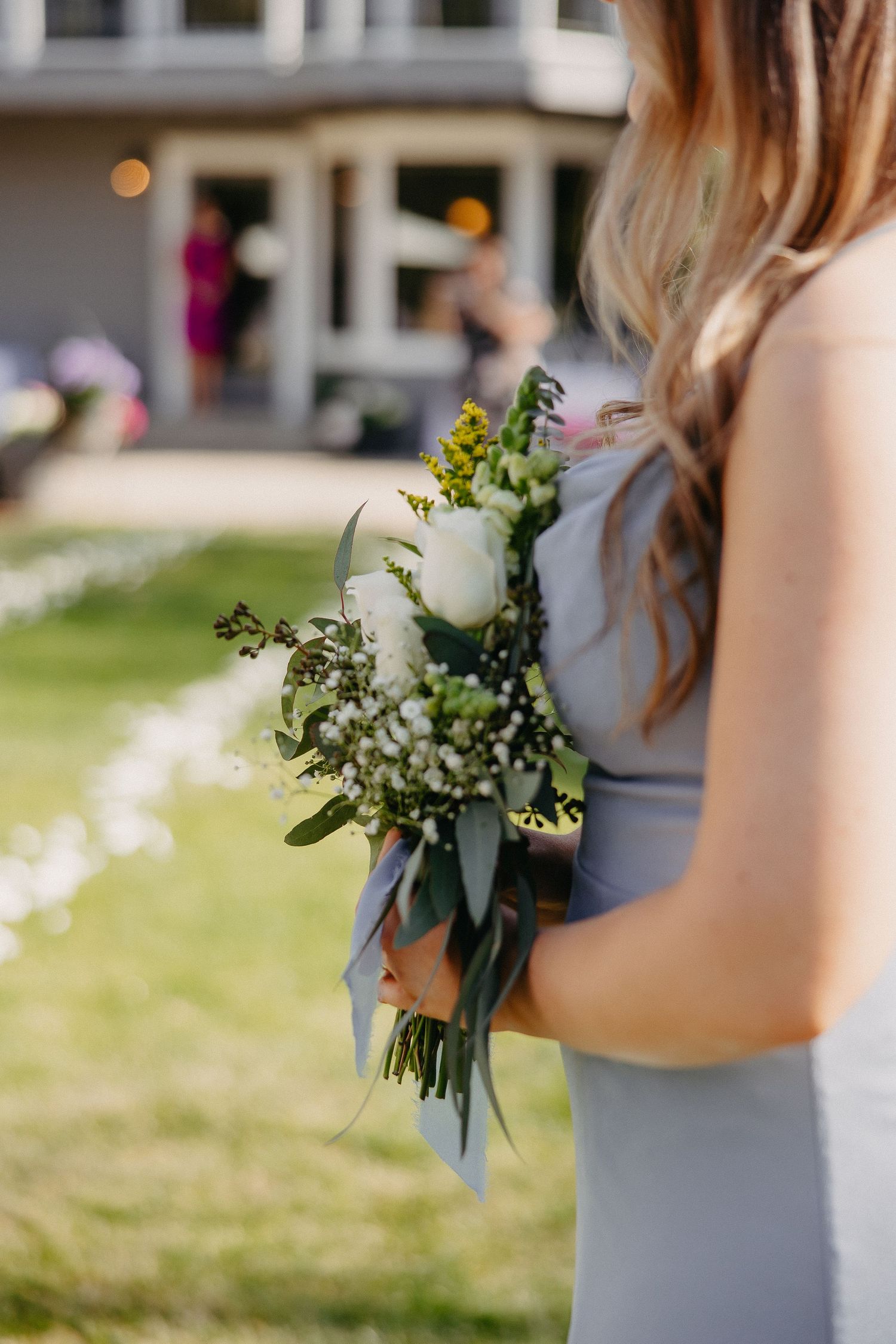 Bridesmaid holding elegant white and green floral bouquet with blue ribbon.