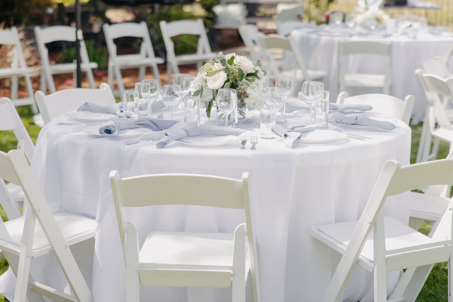 Elegant white wedding reception table setup with folding chairs and delicate floral centerpiece.