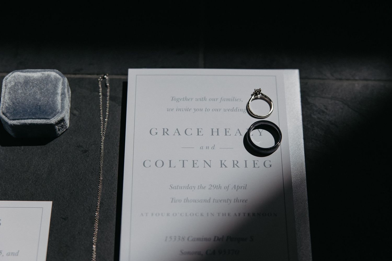 Wedding invitation with ring illustration and gray ring box on dark background.