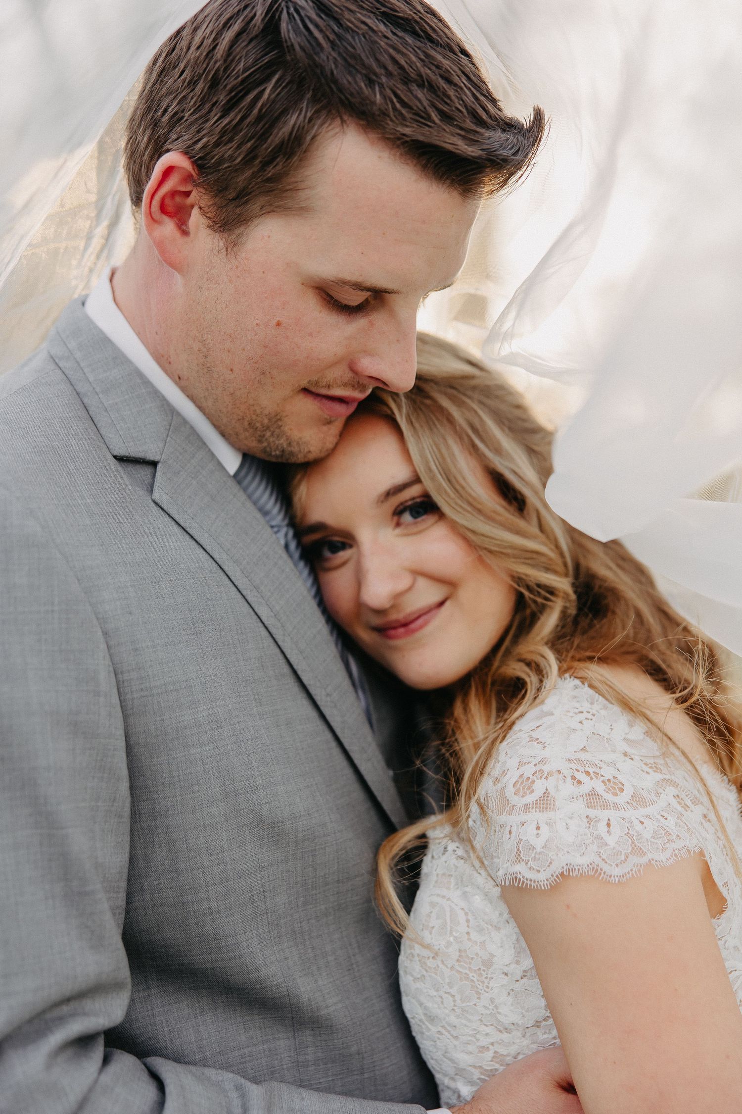 Intimate wedding portrait of a couple in gray suit and white lace dress embracing.