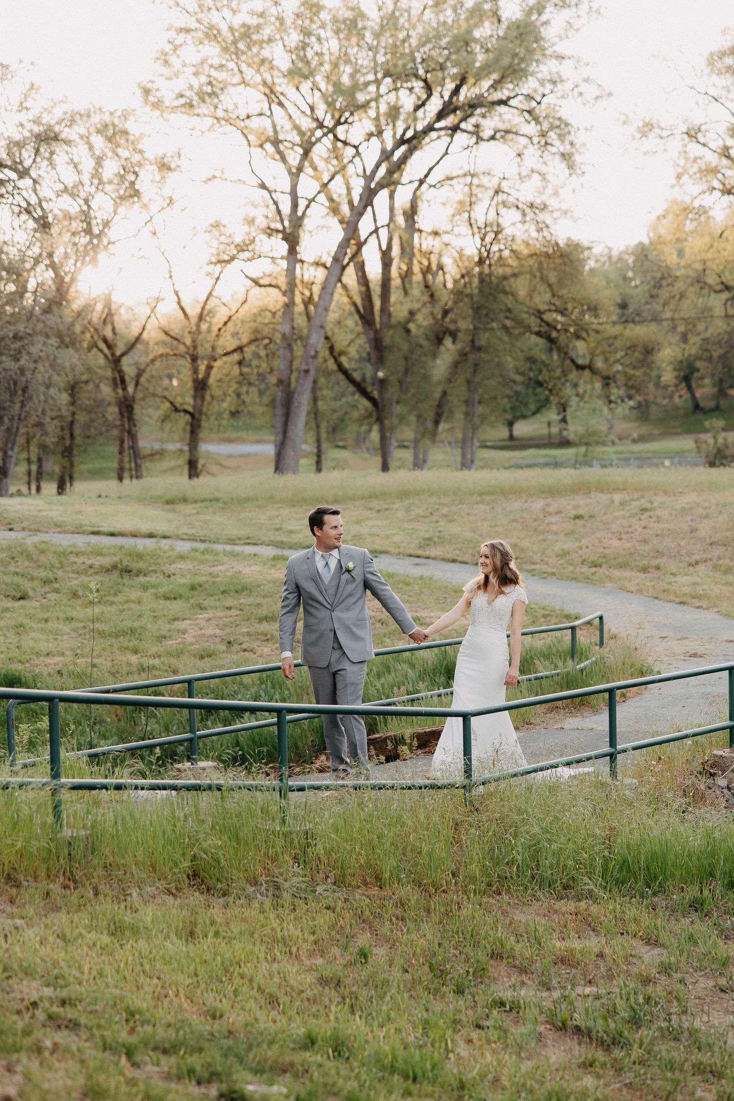 Romantic wedding portrait of couple standing on rustic bridge in pastoral setting.