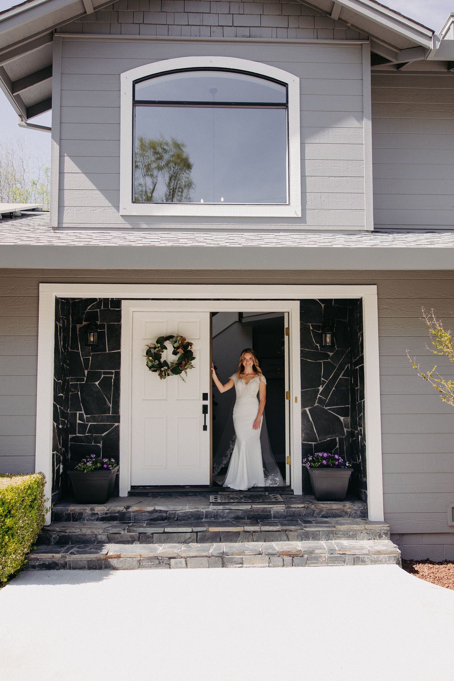 Modern grey house exterior with white door and bridal figure standing in the entrance.