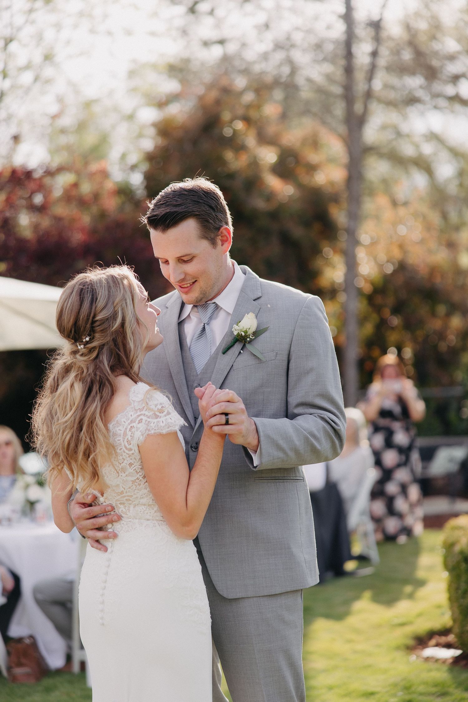Intimate wedding dance moment captured in golden sunlight with autumn trees in background.