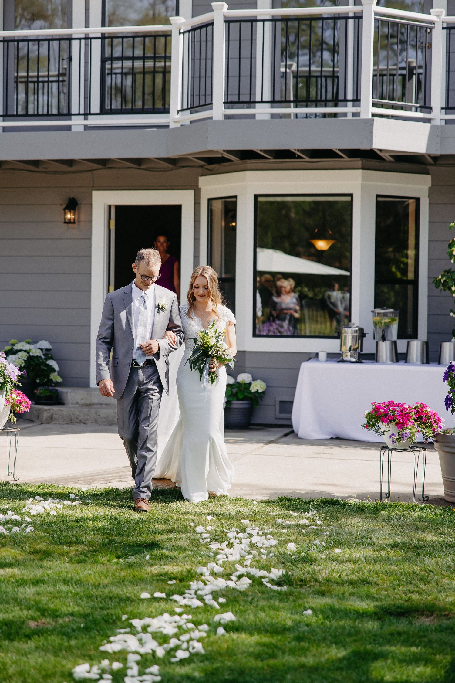 A wedding procession walking past decorated tables on a lawn with white flower petals.