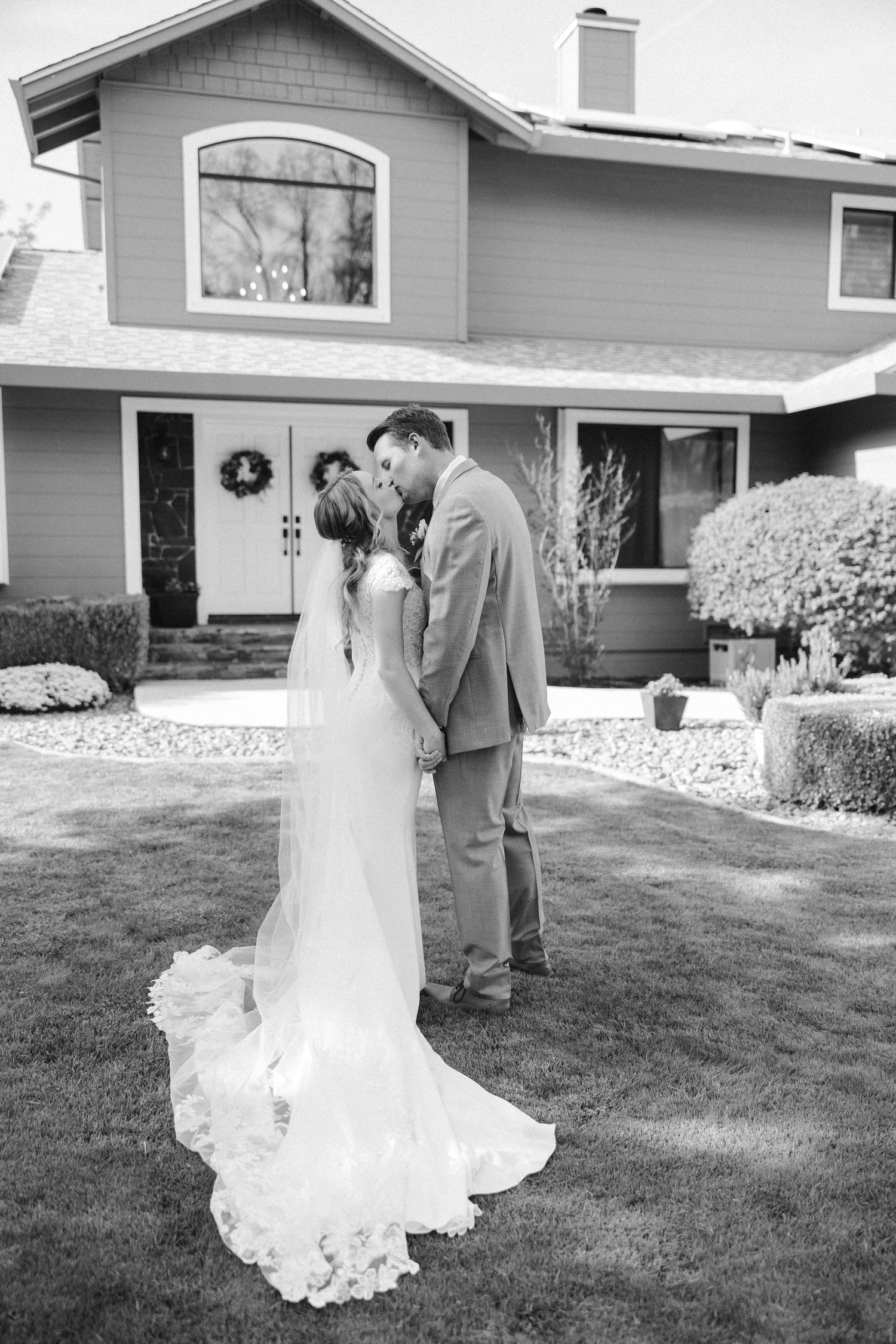 Black and white photo of a romantic wedding moment in front of a house with decorative wreaths.