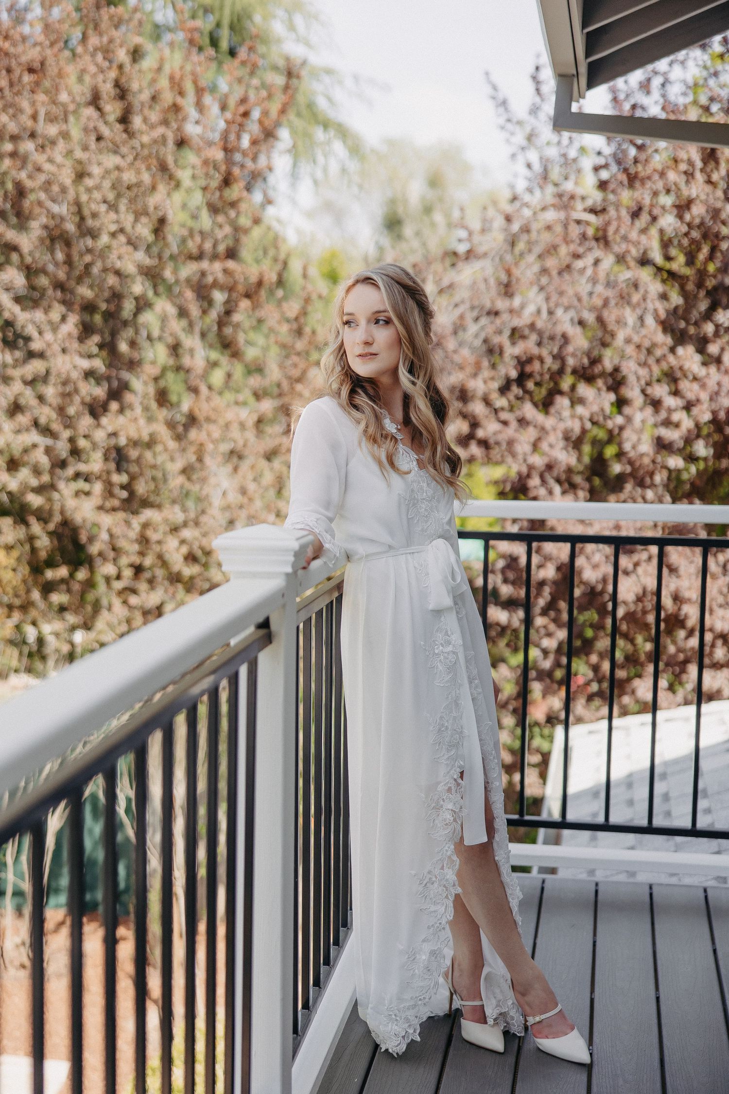 Bridal portrait on deck with autumn foliage wearing lace trimmed white robe.