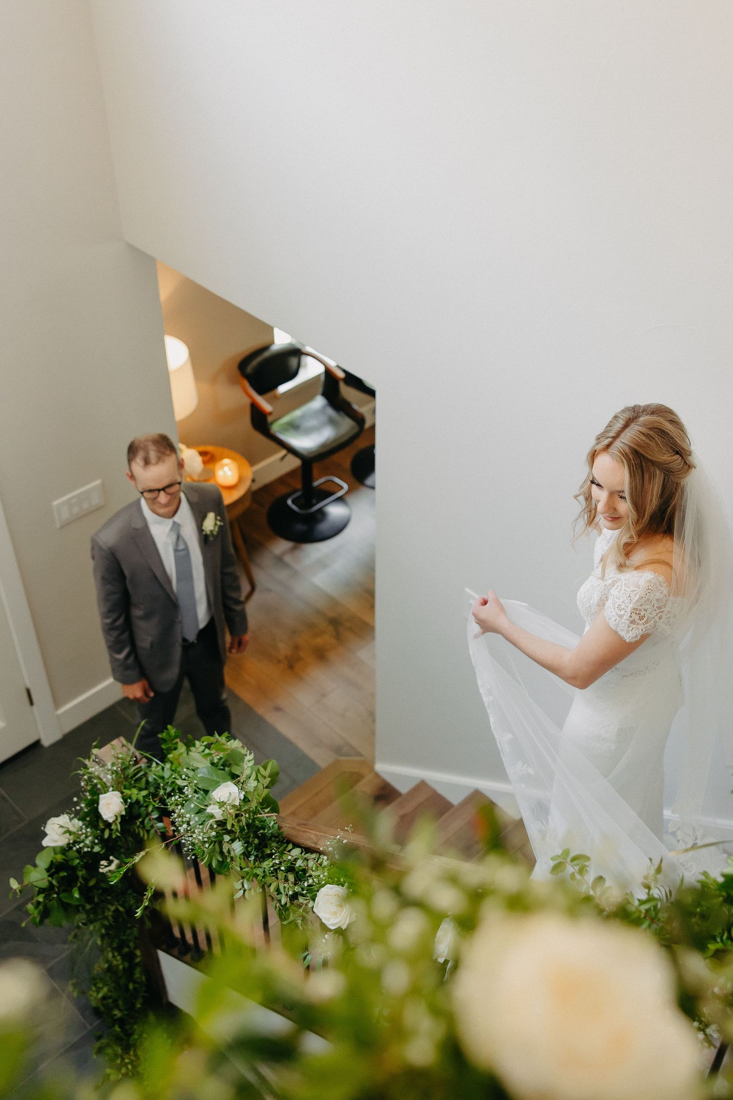 Wedding couple stands on different levels of a staircase decorated with elegant floral arrangements.