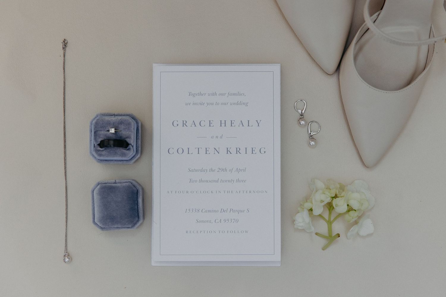 Minimalist wedding stationery layout with blue ring boxes and small white flowers.