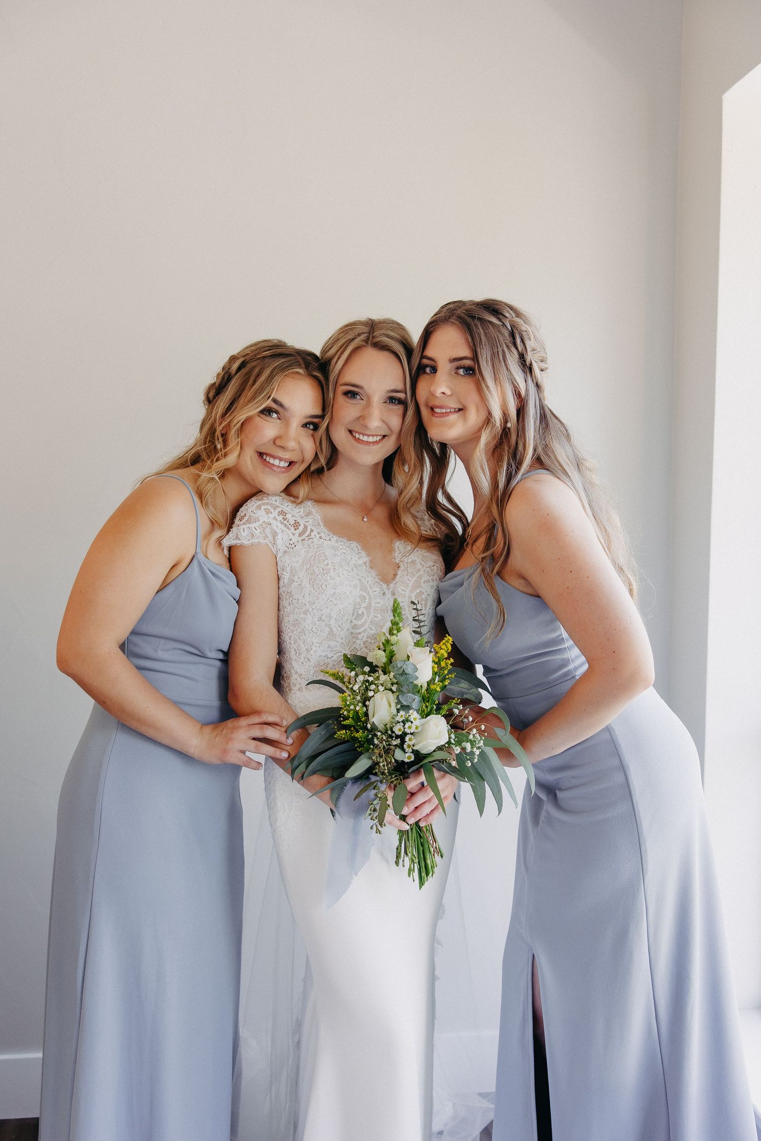 Wedding party poses together with bride in white and bridesmaids in powder blue dresses holding bouquets.