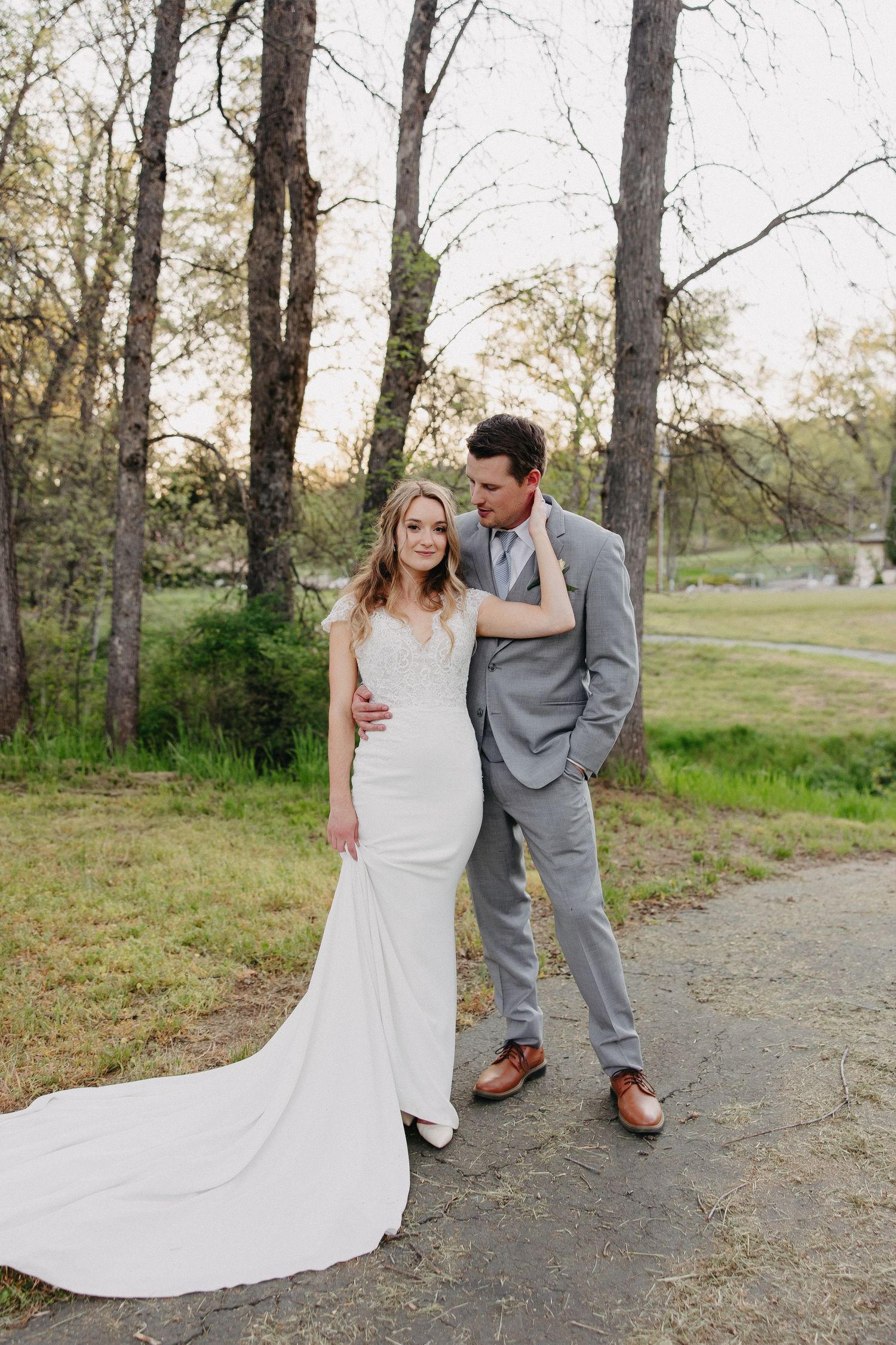 Wedding couple poses on nature path with bride's dress train flowing behind her.