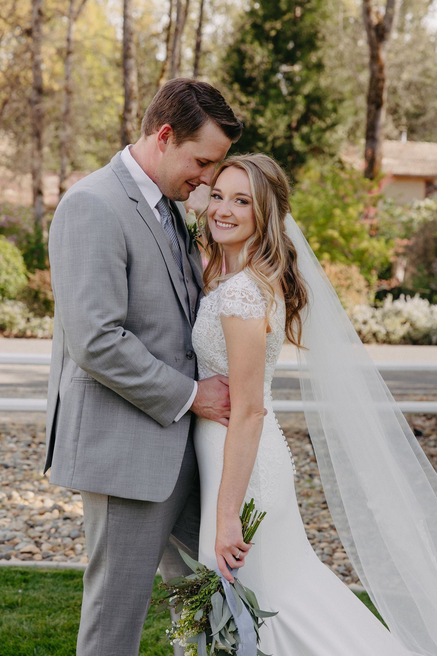 A couple in wedding attire embraces while sharing a tender moment in a garden setting.