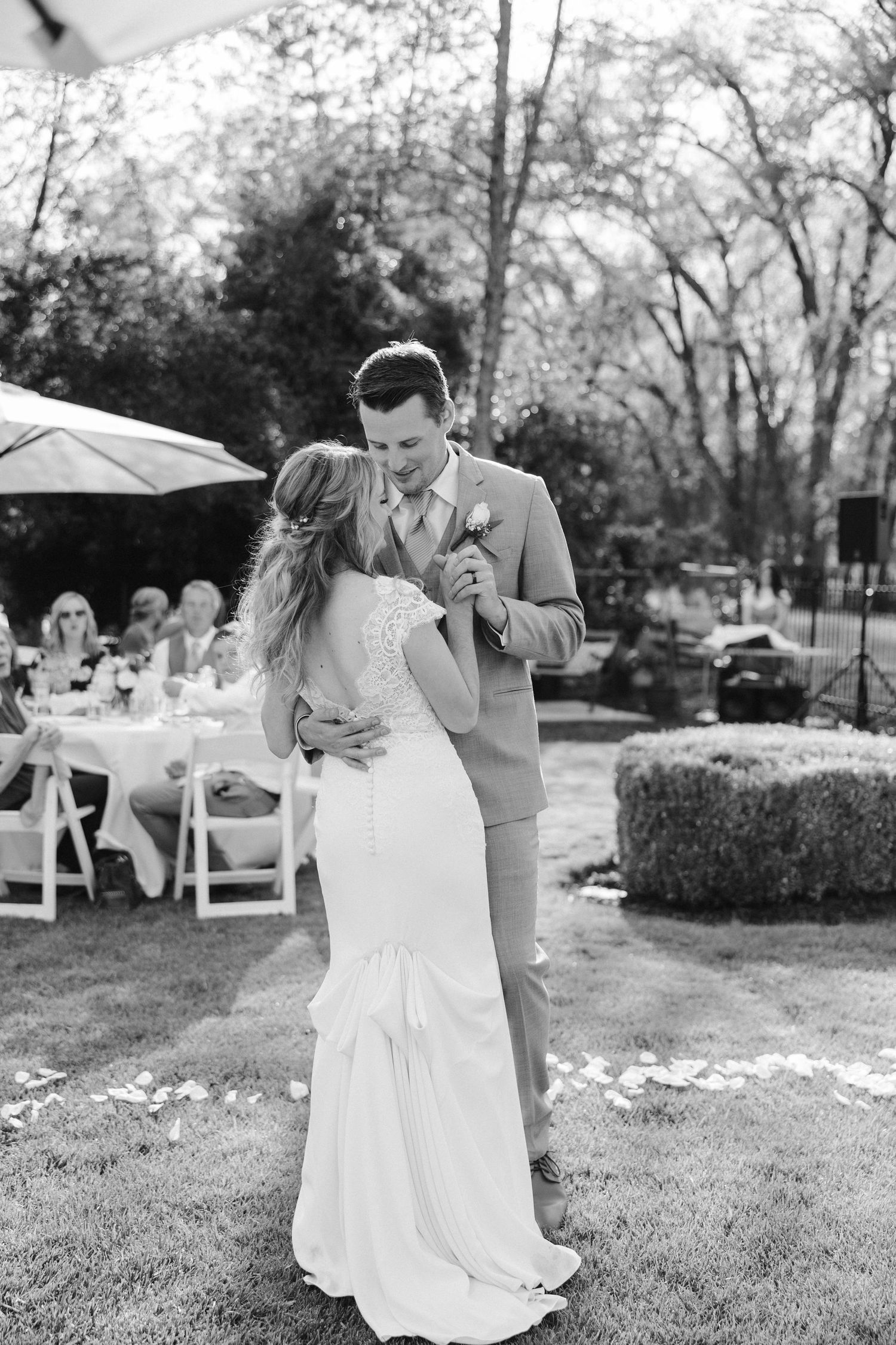 Black and white capture of wedding couple's first dance outdoors with guests seated nearby.