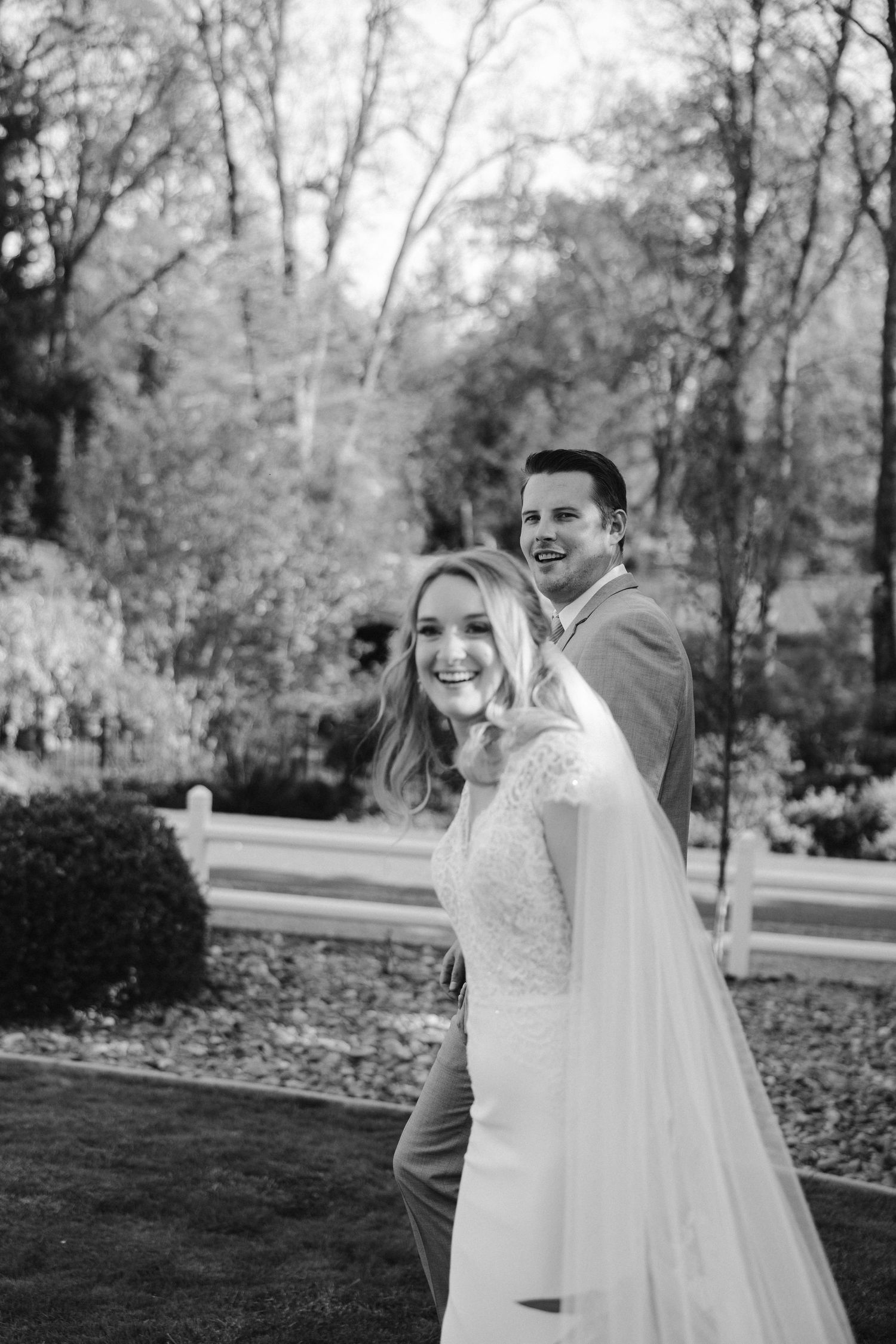 A candid black and white portrait of a happy couple on their wedding day in a garden setting.
