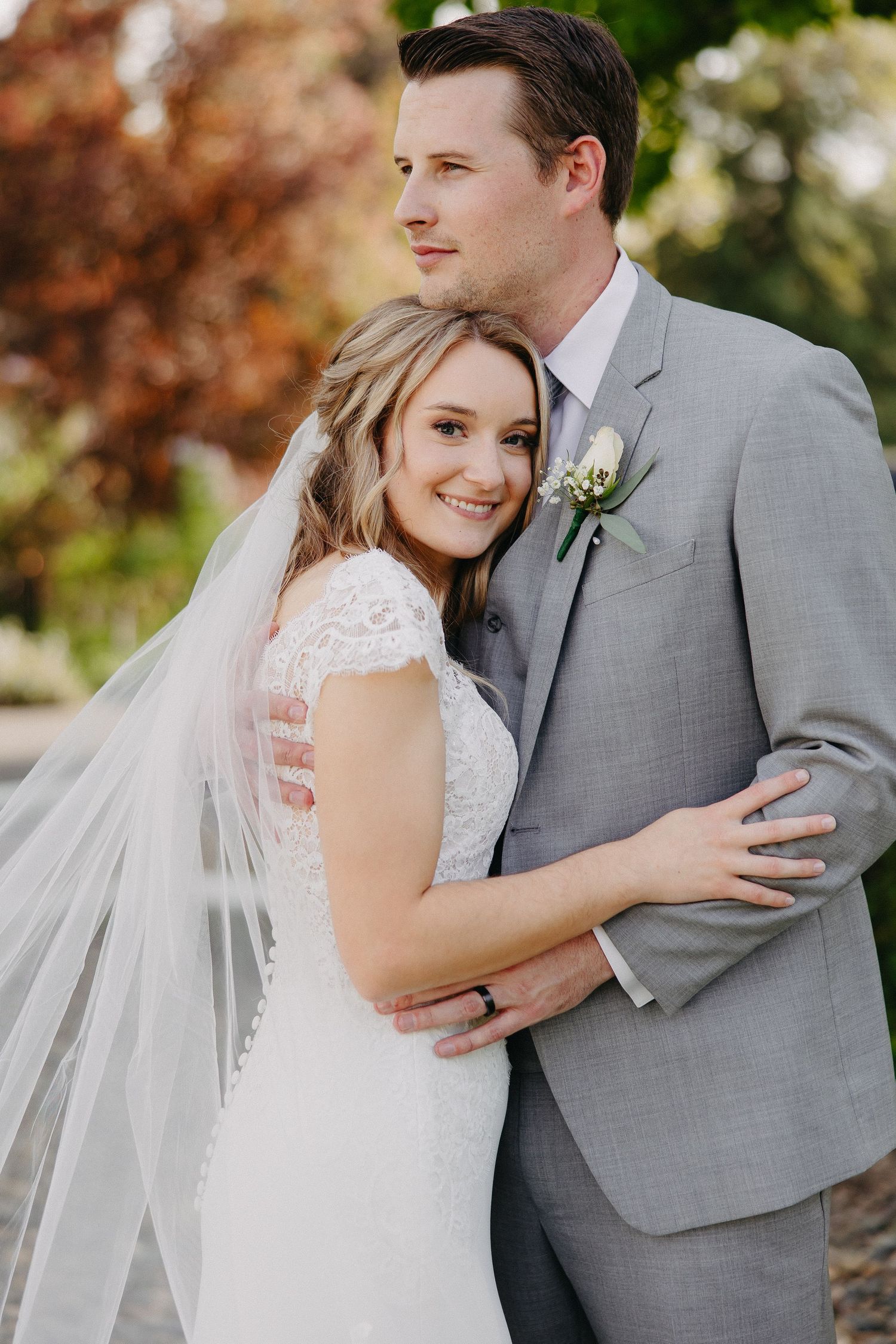 A tender wedding portrait of a couple in elegant attire with the bride wearing a lace dress and flowing veil.