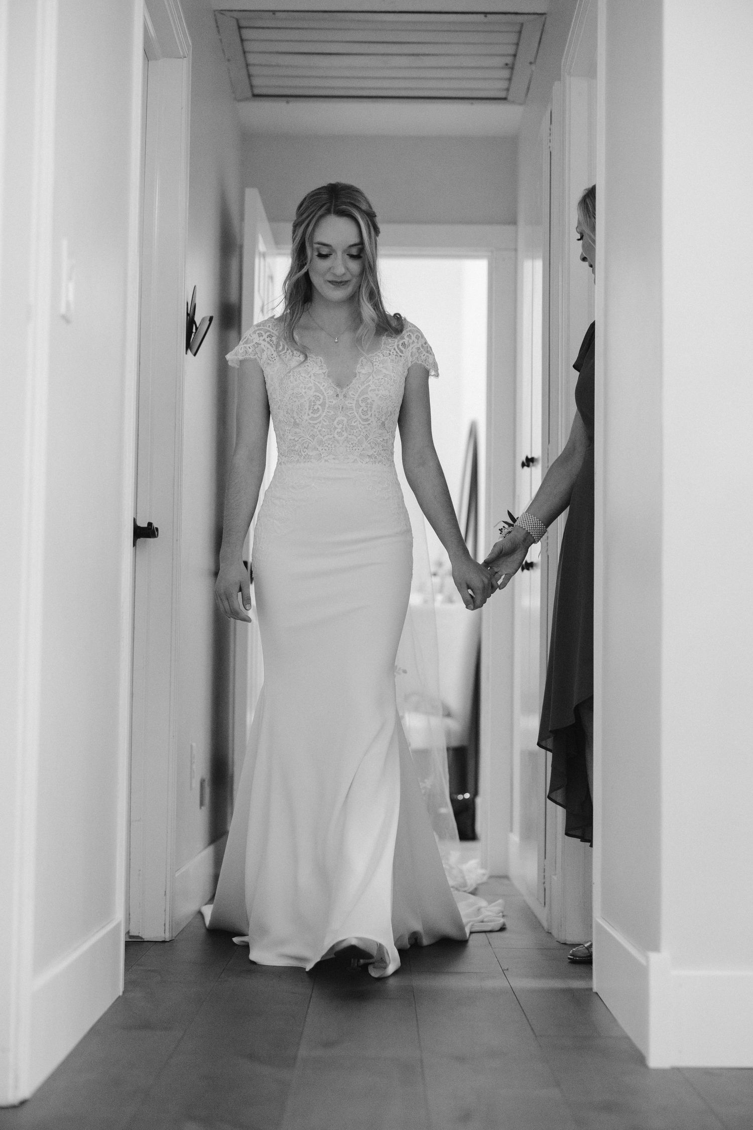 Bride walks gracefully down a hallway in a fitted white wedding gown with lace details.